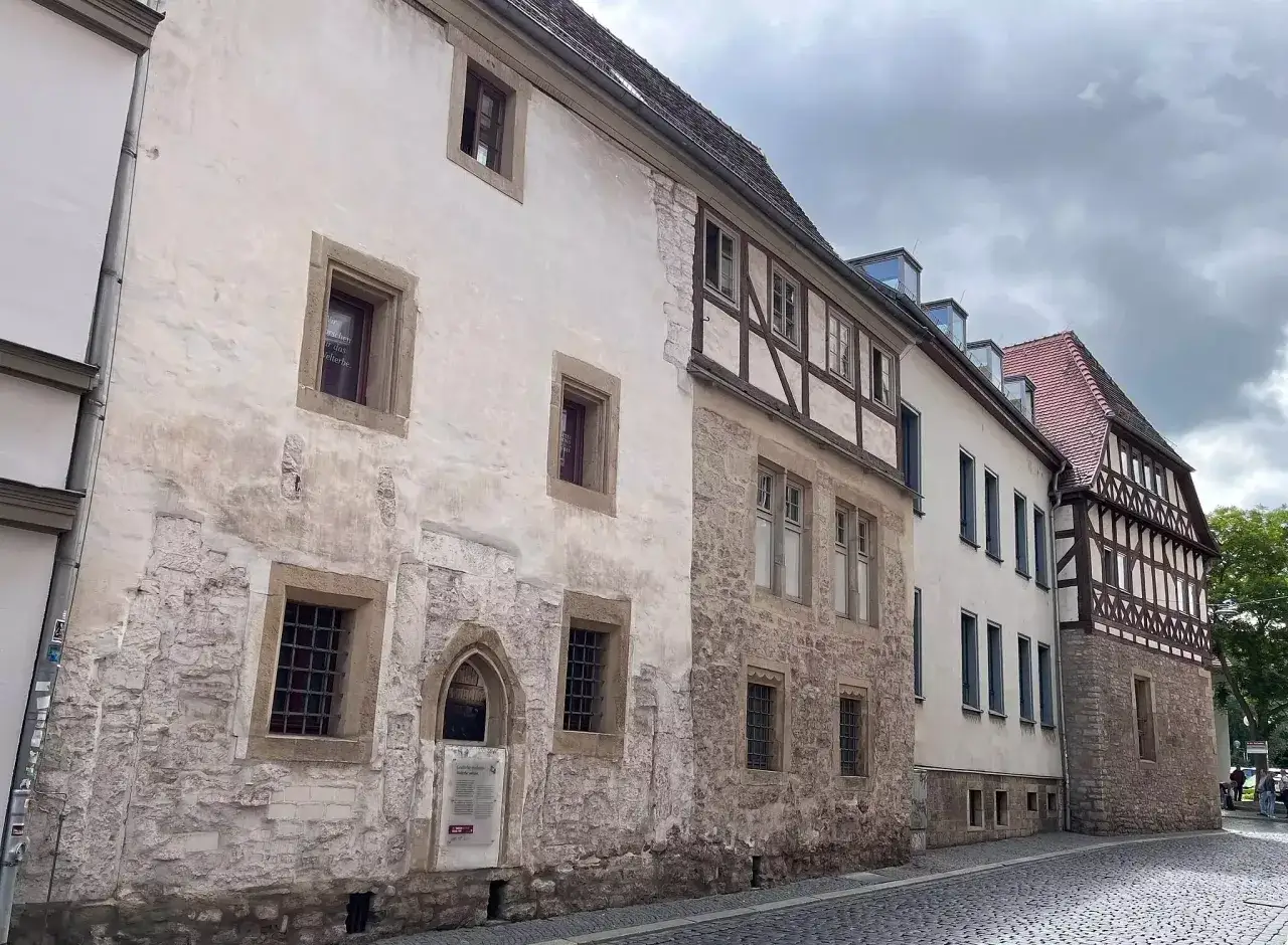 Alte Fachwerkh&auml;user und Steingeb&auml;ude s&auml;umen eine Kopfsteinpflasterstra&szlig;e. Ein Schild deutet auf die Geschichte der Juden im Mittelalter hin.