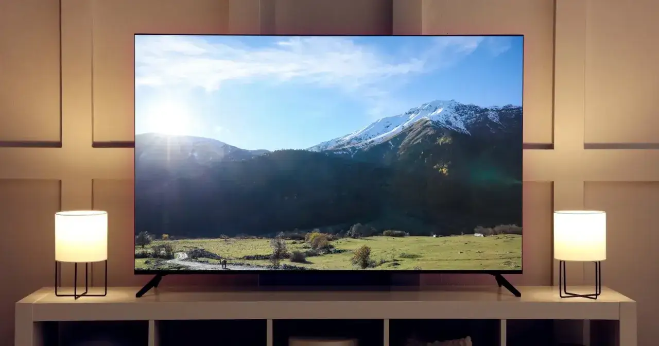Wielki telewizor 75 cali wyświetla słoneczny krajobraz górski. Dwie lampki nocne oświetlają mebel pod ekranem.