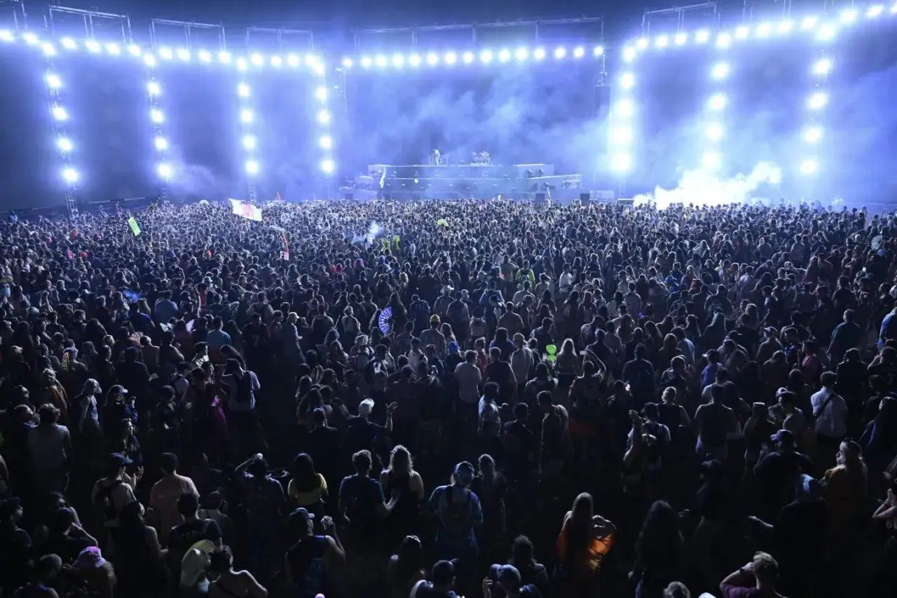 Riesige Menge feiert bei einem EDM-Musikfestival. Die Lichter der Bühne erhellen den Himmel, während die Menge tanzt. Das EDM-Musik-Meaning ist hier die kollektive Freude und Energie.