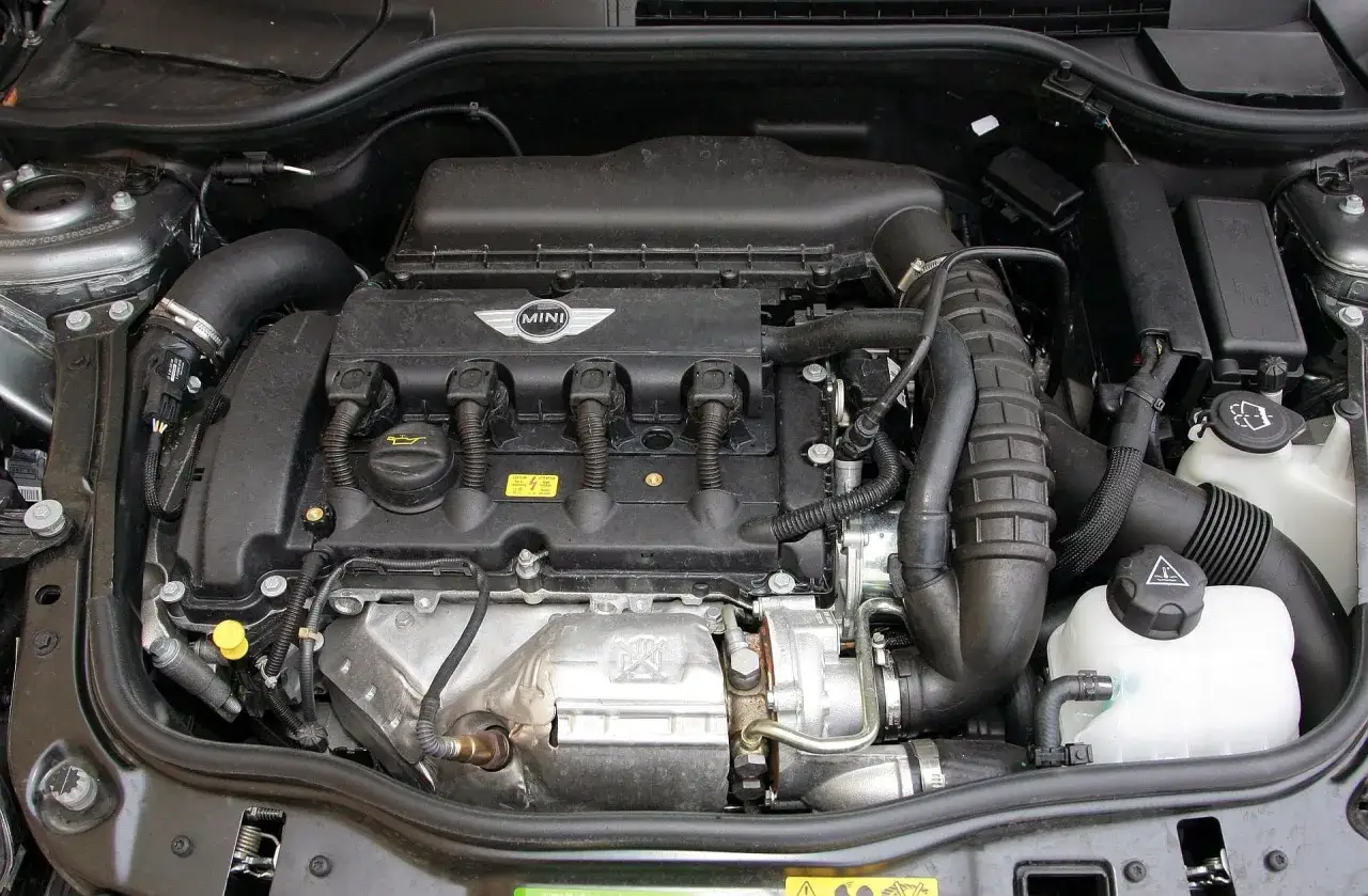 Silnik Mini R58 z turbosprężarką, widoczne przewody, zbiornik płynu i logo Mini.