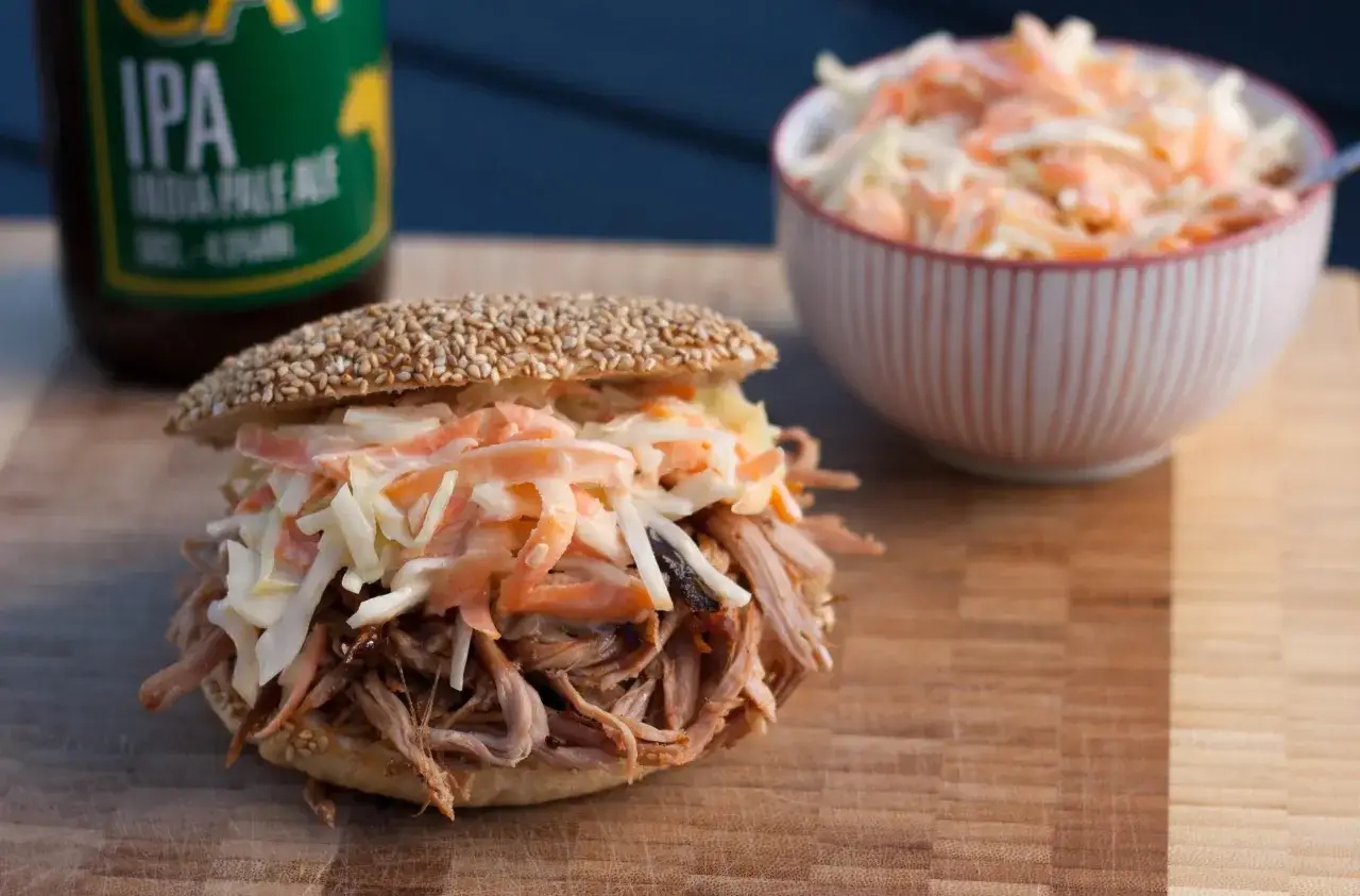 Pulled Pork Sandwich mit Coleslaw, perfekt für ein schnelles pulled pork rezept. Daneben eine Schüssel mit Coleslaw und eine IPA-Flasche.