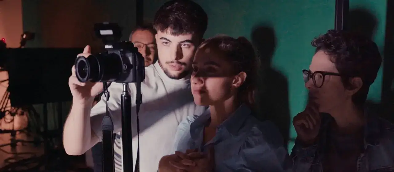 Jóvenes aprendiendo comunicación audiovisual, con un chico operando una cámara y otros observando.