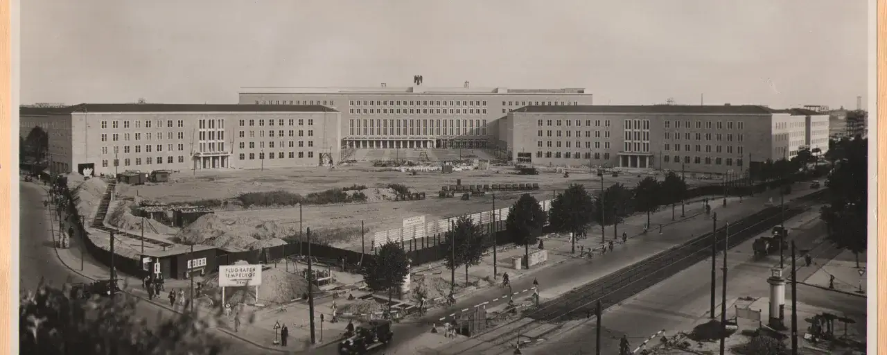 Gro&szlig;es Geb&auml;ude mit vielen Fenstern, Baustelle davor. Ein Schild weist den Weg zum Flughafen Tempelhof.