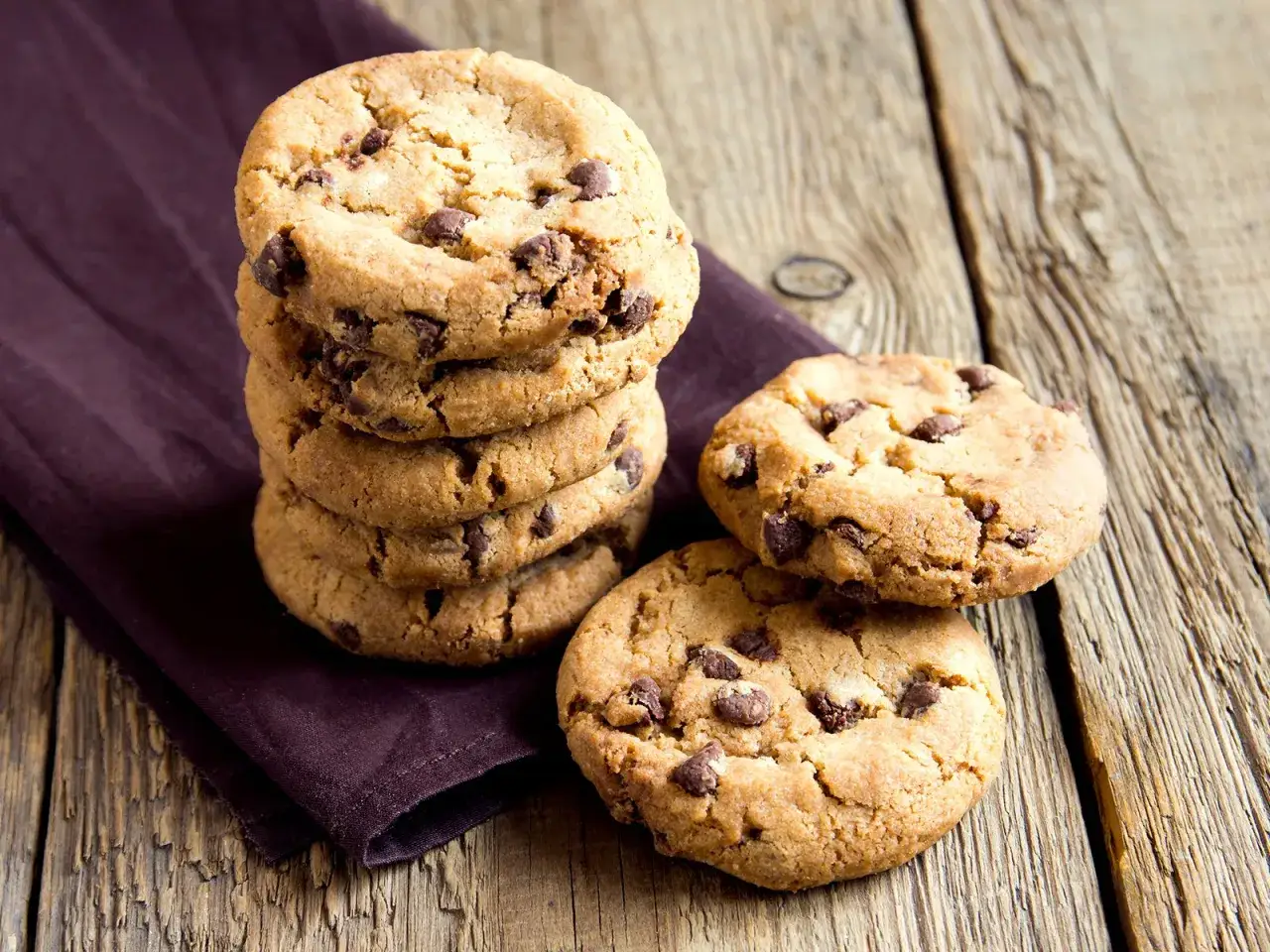 Ein Stapel Schokoladenkekse auf einem dunklen Tuch, daneben zwei weitere Kekse. Perfekt für ein schnelles Cookies Rezept.