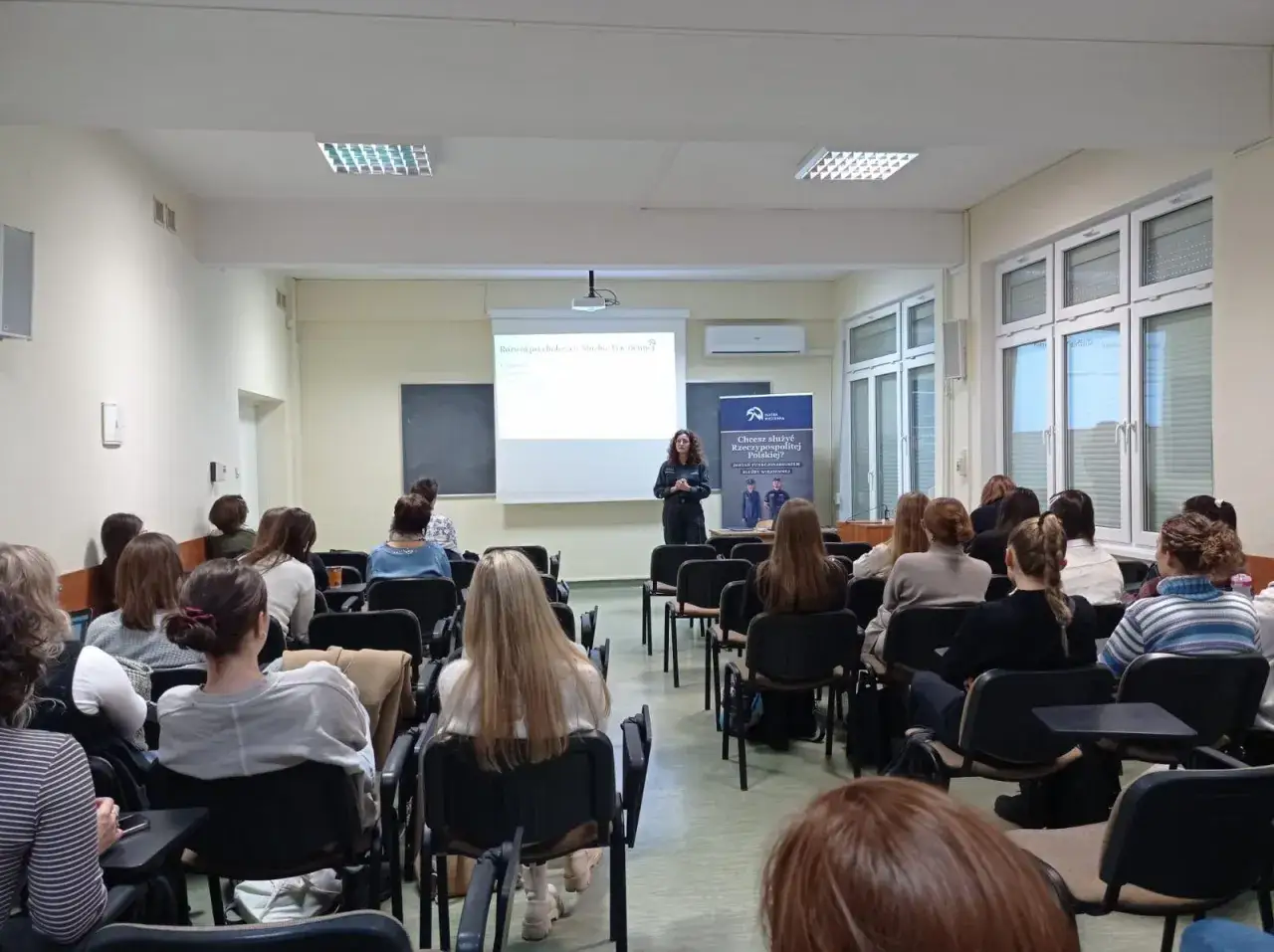 Wykład o psychologii penitencjarnej. Prelegentka mówi do grupy słuchaczy w sali wykładowej.