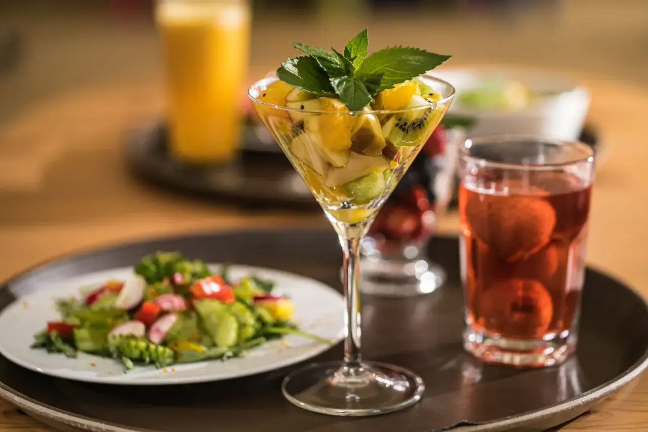 Pyszny deser owocowy z kiwi i pomarańczy, idealny na dietę dąbrowskiej. Obok sałatka i napój.