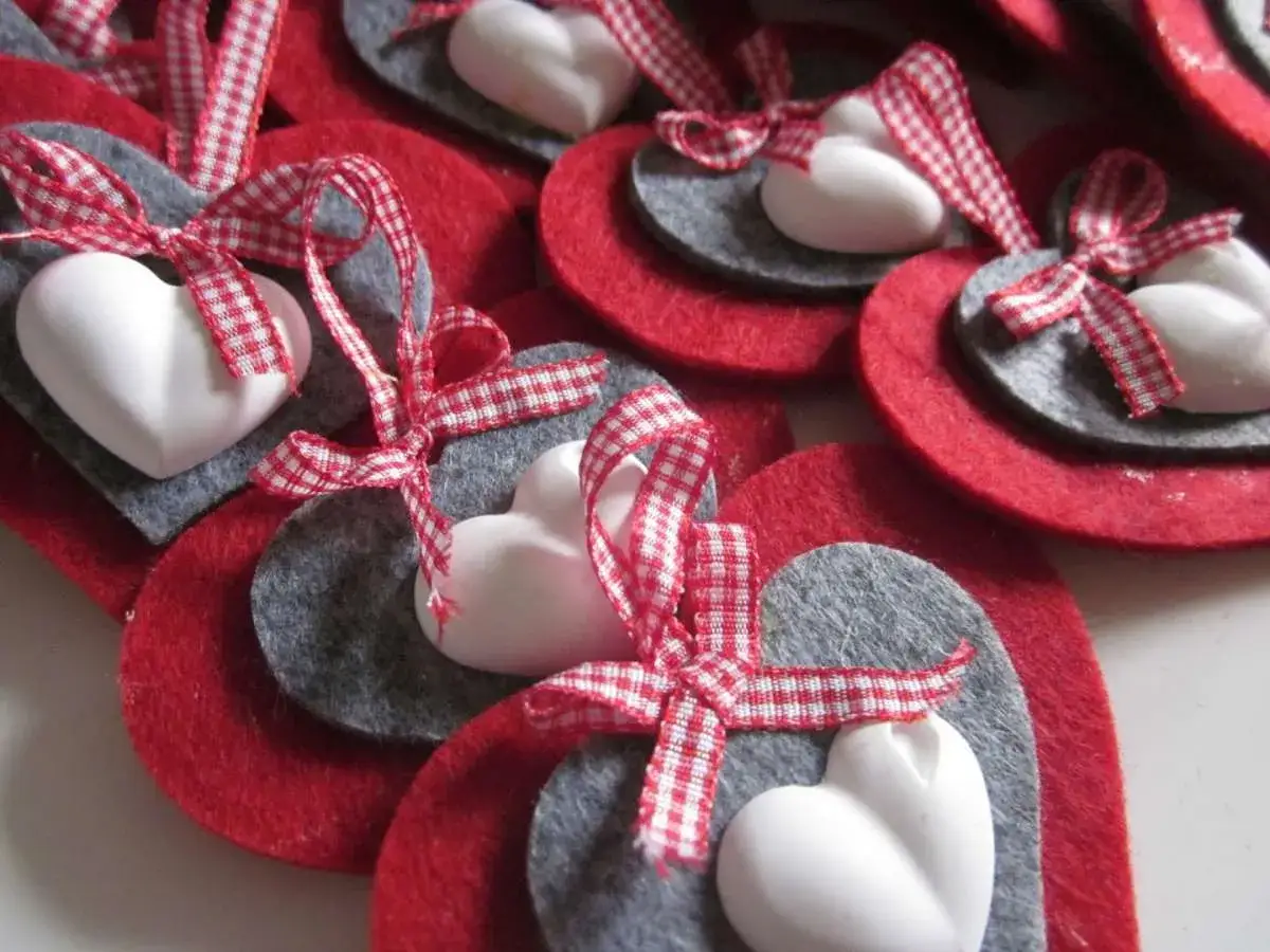 Cuori rossi e grigi di **fogli di feltro**, decorati con fiocchi a quadretti e piccoli cuoricini bianchi.