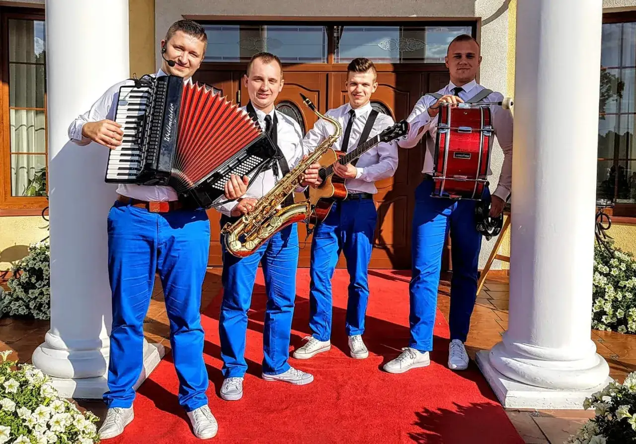 Zespół muzyczny grupa speed w strojach z niebieskimi spodniami i białymi koszulami, gotowy do występu z akordeonem, saksofonem, gitarą i bębnem.