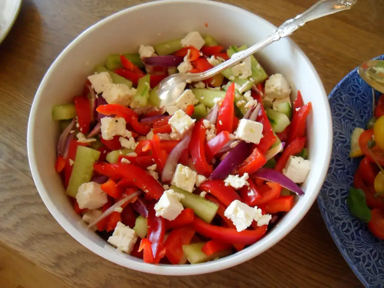 En sk&aring;l med sopska salata, full av f&auml;rsk paprika, gurka, r&ouml;dl&ouml;k och fetaost. En sked ligger i sk&aring;len.