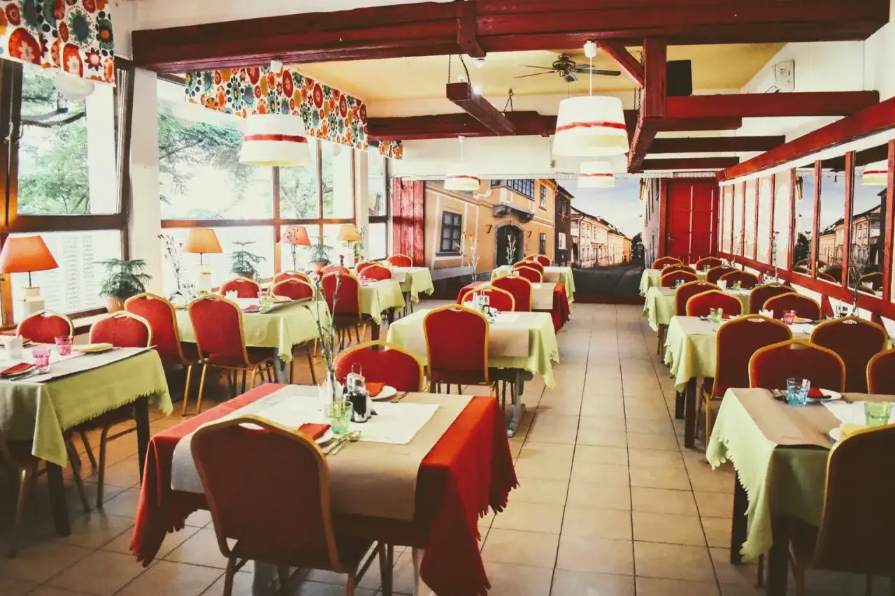 Przytulna restauracja z czerwonymi krzesłami i stolikami nakrytymi na przyjęcie. W tle mural przedstawiający ulicę, jakby z Gdańska, gdzie można poczuć klimat czardasz.