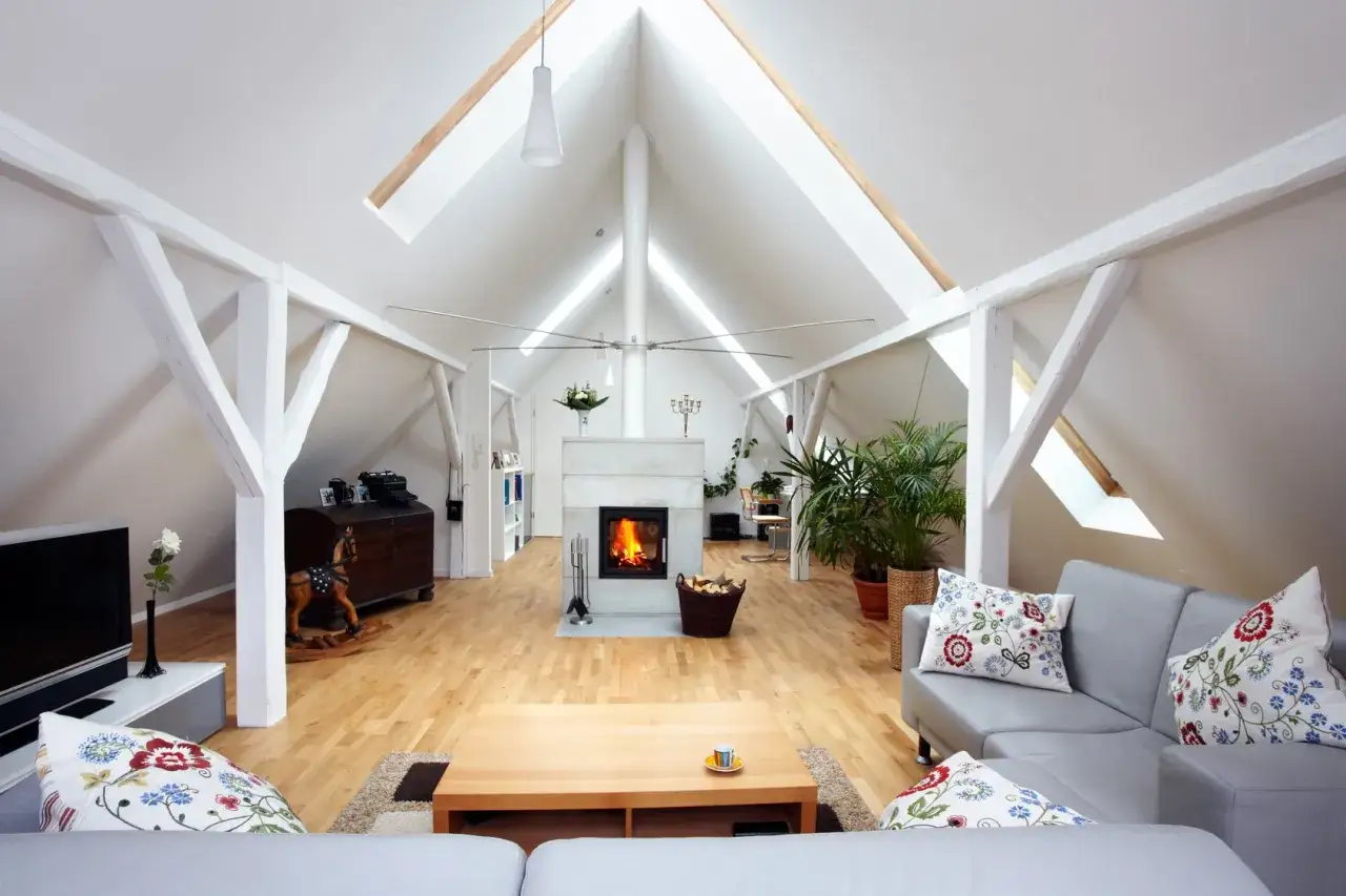 Aménagement comble 30m2 : salon cosy avec cheminée, canapé gris, parquet clair et poutres apparentes.