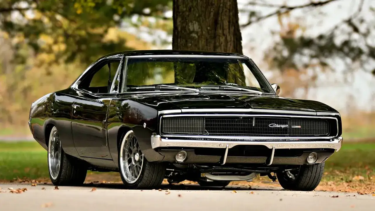 Svart amerikansk sportbil, en klassisk Dodge Charger, parkerad vid ett tr&auml;d.
