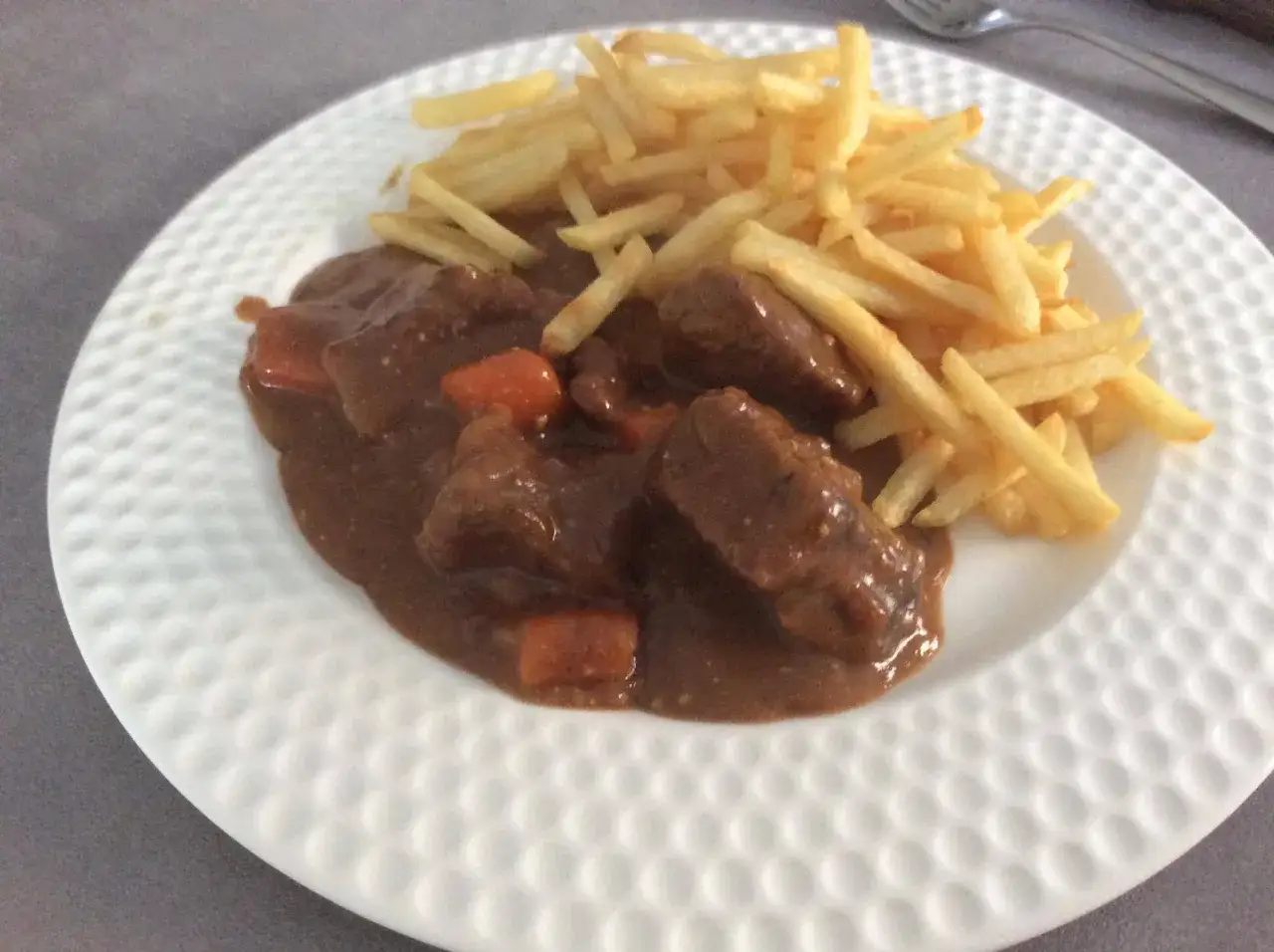 Carbonade flamande cookeo : un plat savoureux de viande mijot&eacute;e dans une sauce brune, accompagn&eacute; de frites dor&eacute;es sur une assiette blanche.