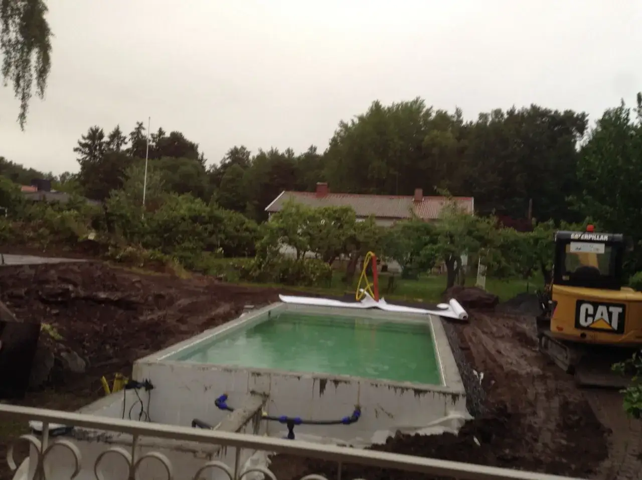 Byggnation av en pool i sluttning. En grävmaskin står redo bredvid den nyligen fyllda poolen.