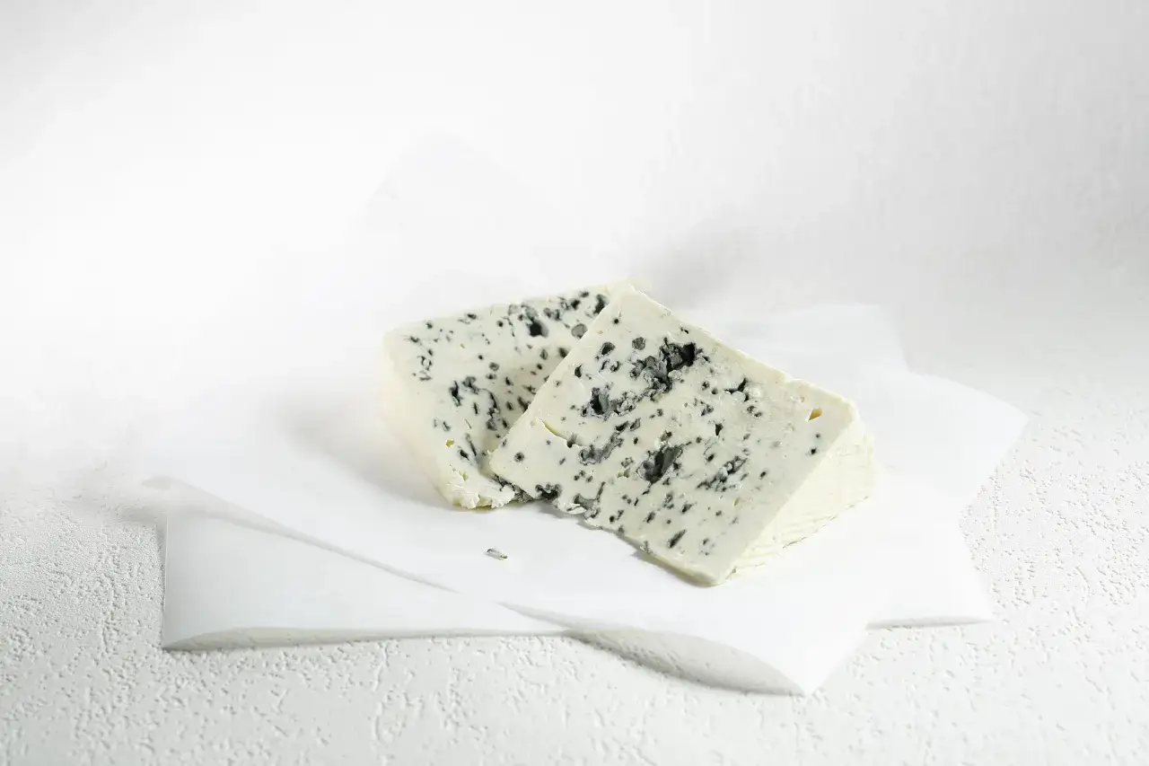 Deux morceaux de Saint Agur, un fromage crémeux aux veines bleues intenses, posés sur du papier blanc.