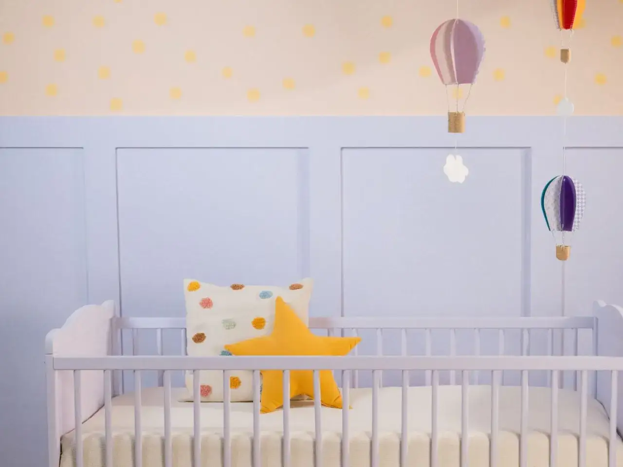 Ein frisch gestrichenes Kinderbett in zartem Lila, dekoriert mit einem Sternkissen und bunten Hei&szlig;luftballons.