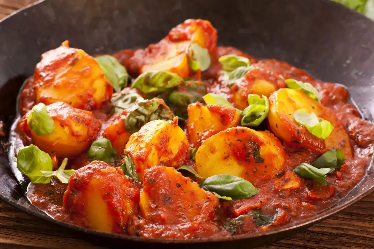 Patate al sugo, un delizioso contorno per carne alla pizzaiola, guarnite con basilico fresco.