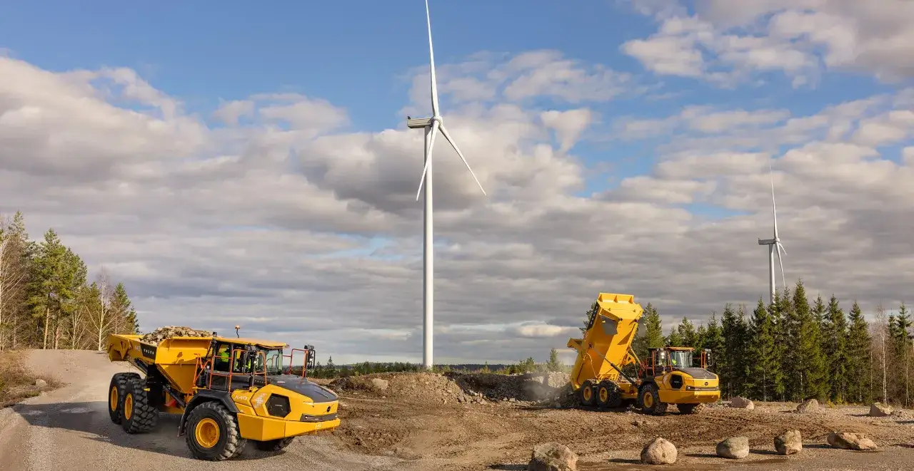 Dwie żółte wywrotki Volvo A30D pracują na budowie farmy wiatrowej. Dane techniczne tych maszyn pozwalają na efektywną pracę w trudnym terenie.