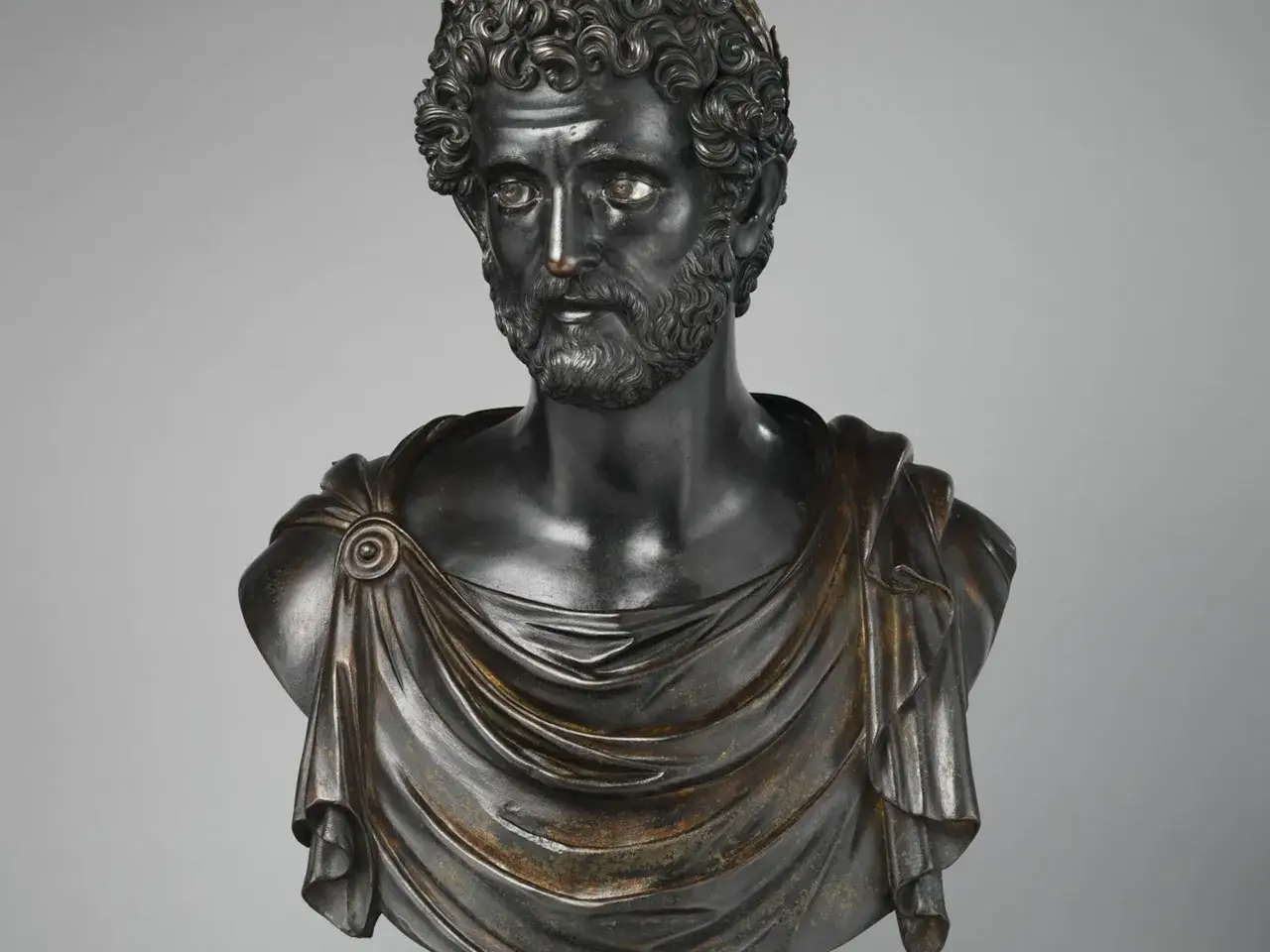 Bronzebüste eines Mannes mit Bart und lockigem Haar, gekleidet in eine Toga. Er könnte der Dichter Ovid sein, der für seine Metamorphosen bekannt ist.