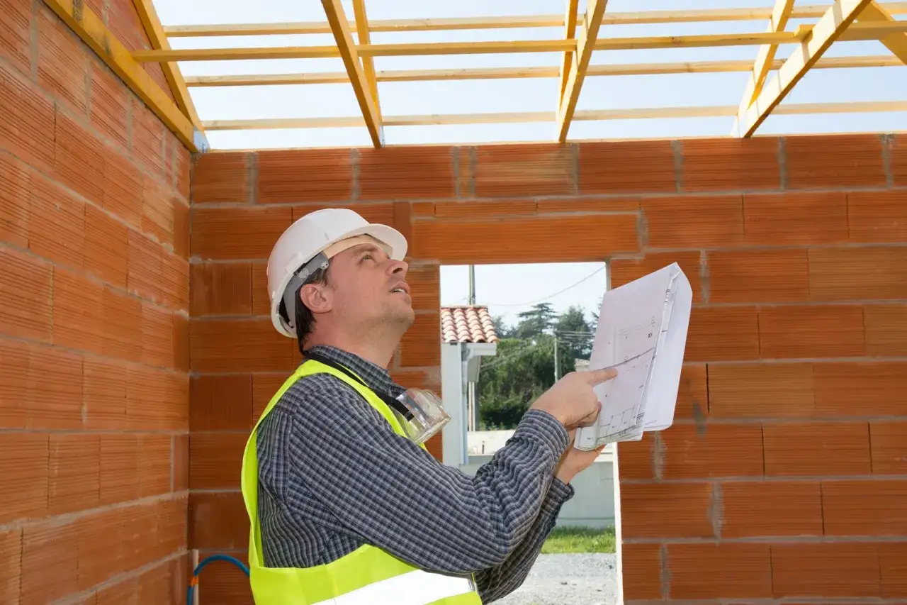 Un ouvrier examine des plans sur un chantier. Il s'assure de la conformité des travaux, même en cas d'intervention d'une autre entreprise, pour la garantie décennale.