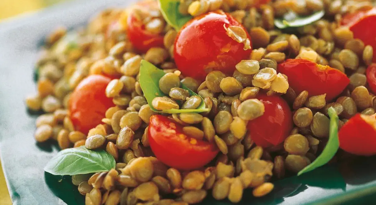 Un'appetitosa insalata di lenticchie con pomodorini ciliegino e foglie di basilico fresco.