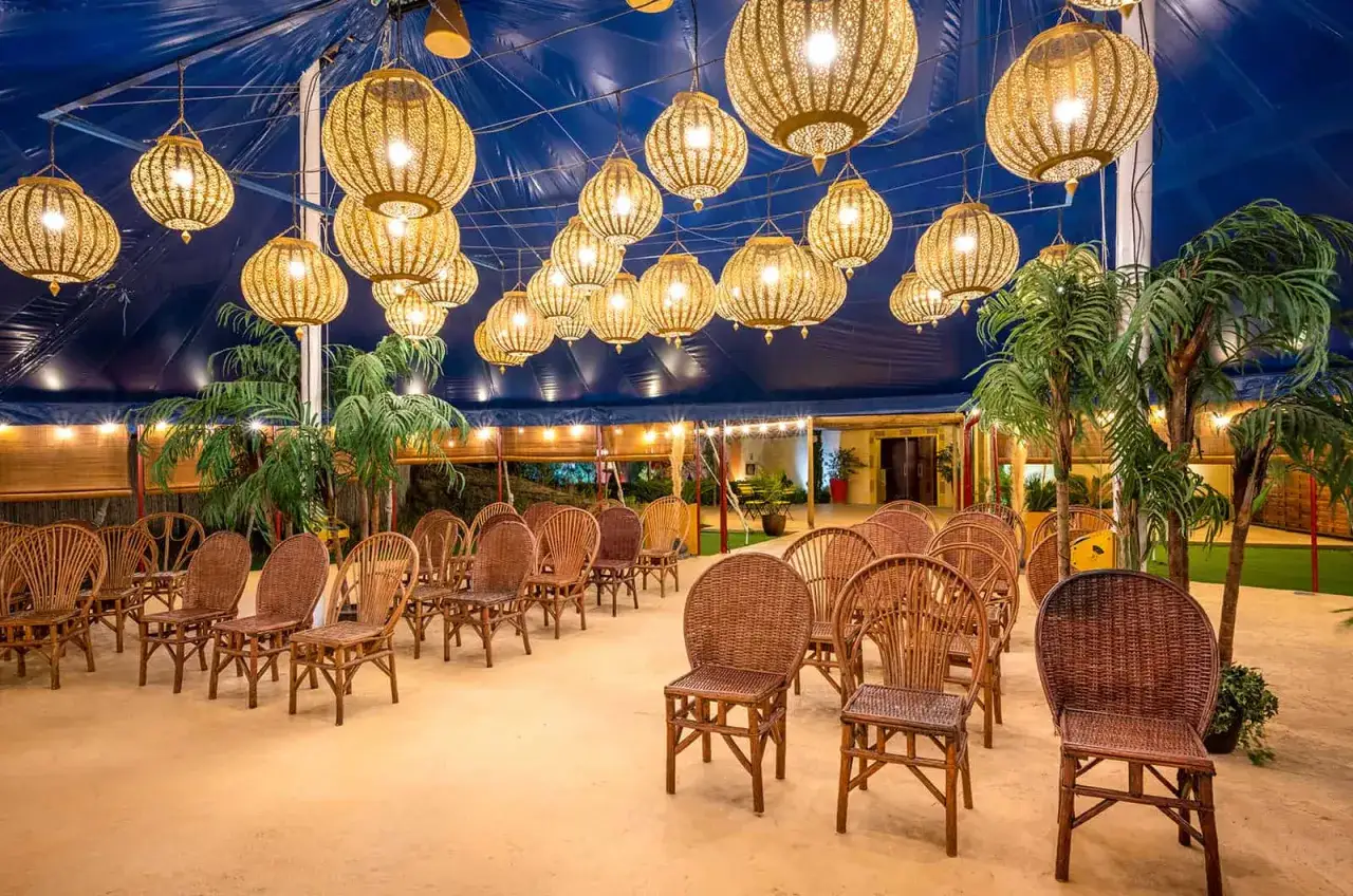 Sillas de mimbre dispuestas para un evento bajo lámparas doradas. Un hermoso escenario para tus sitios de eventos.