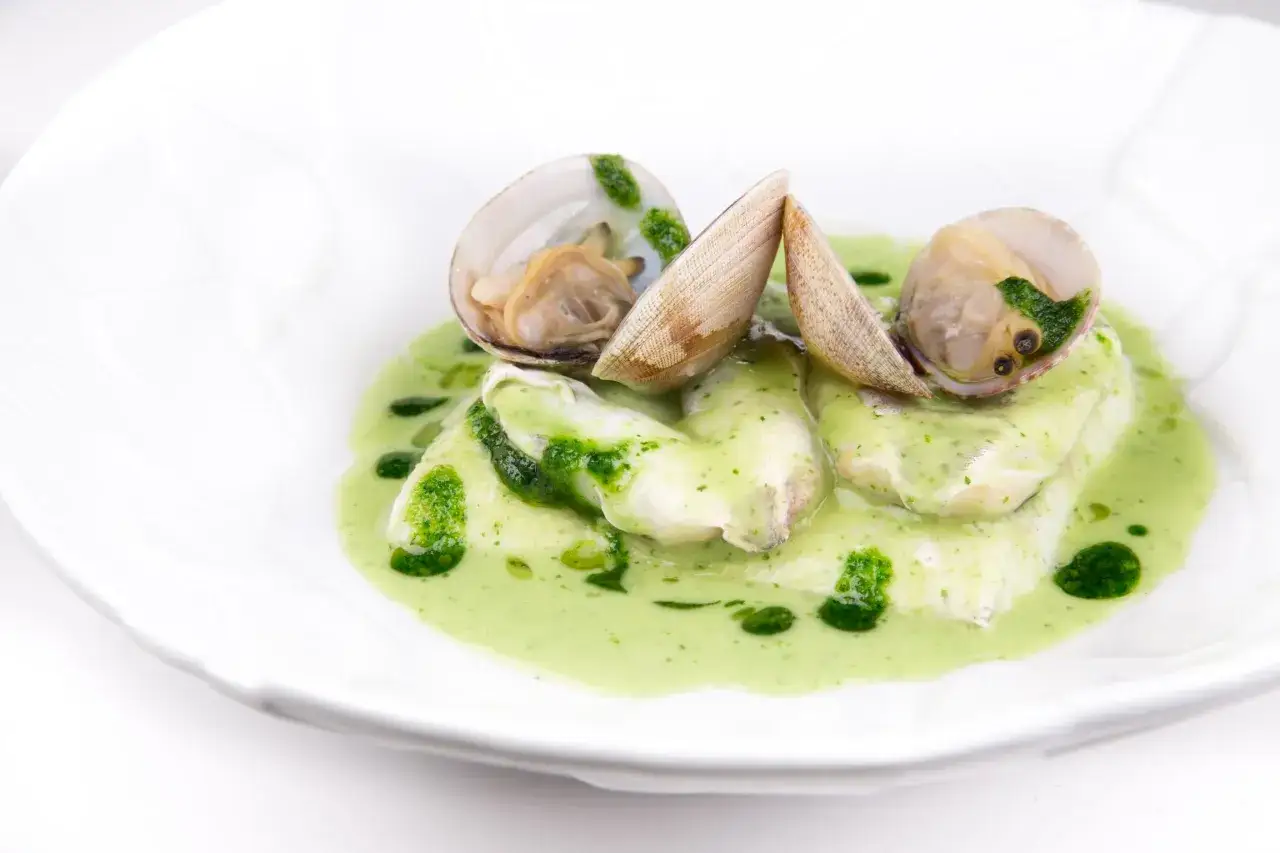 Deliciosas cocochas de merluza en salsa verde, adornadas con almejas frescas. Un plato que evoca el sabor del mar.