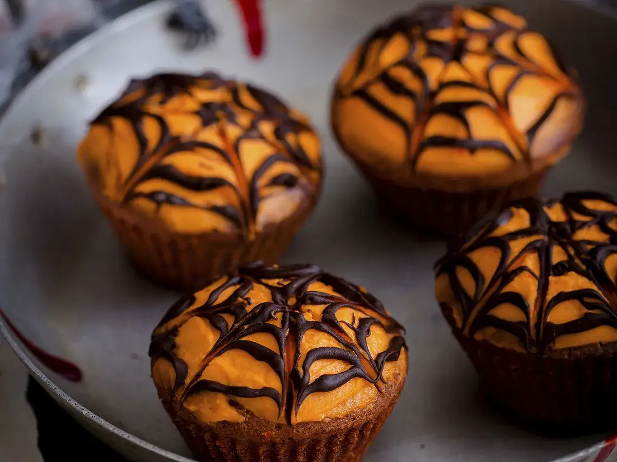 Quatre cupcakes d'Halloween orange vif, d&eacute;cor&eacute;s d'une toile d'araign&eacute;e en chocolat noir. Parfait pour une f&ecirc;te effrayante !
