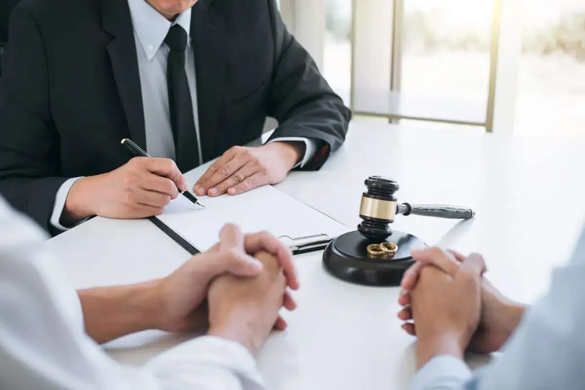Prawnik w garniturze podpisuje dokument, obok młotek sędziowski i obrączki.