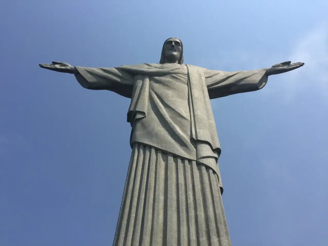 Wielki Jezus w Rio de Janeiro, z rozłożonymi ramionami, wita świat pod błękitnym niebem.