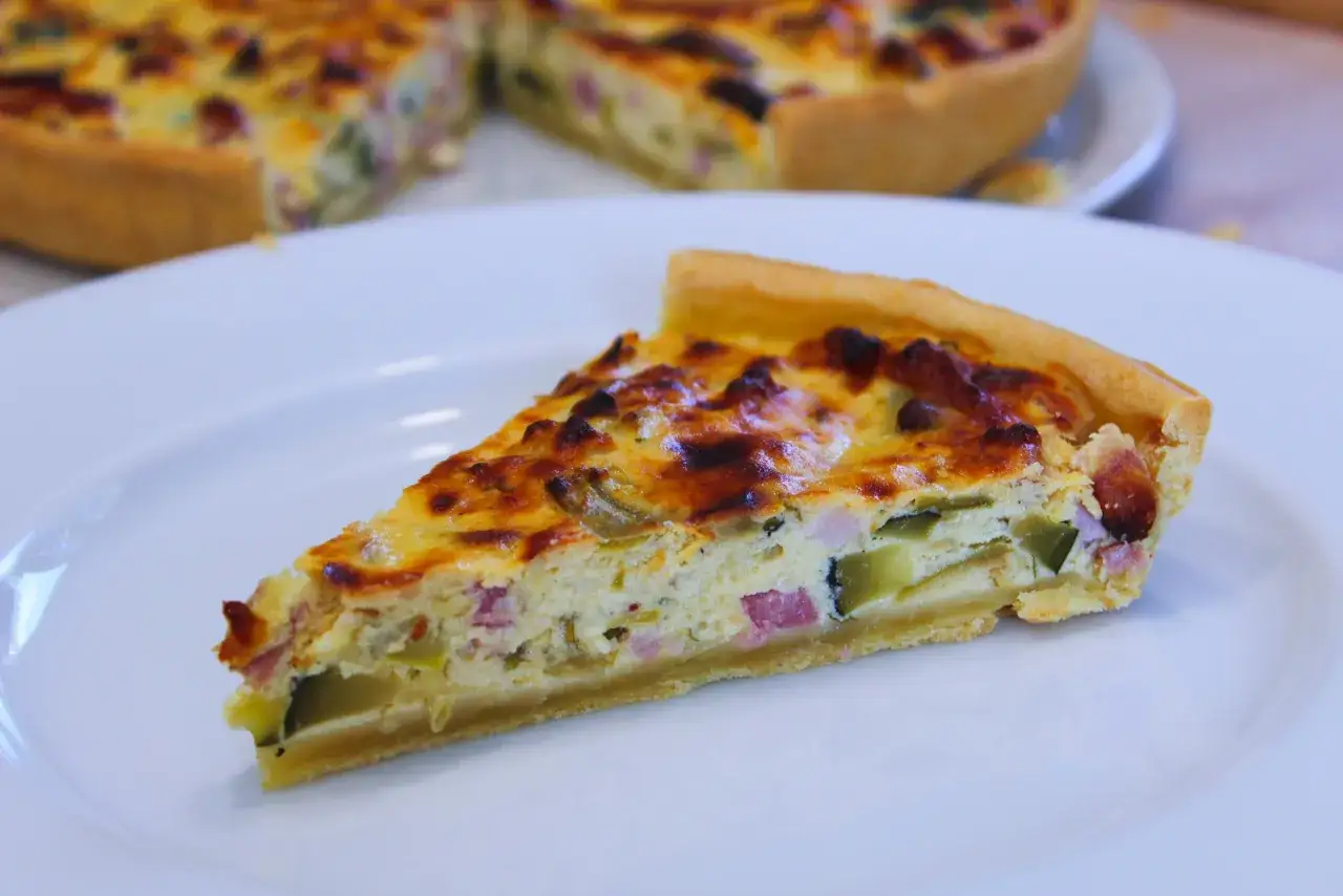Tranche de tarte ricotta courgette, garnie de lardons et de fromage dor&eacute;, servie sur une assiette blanche.