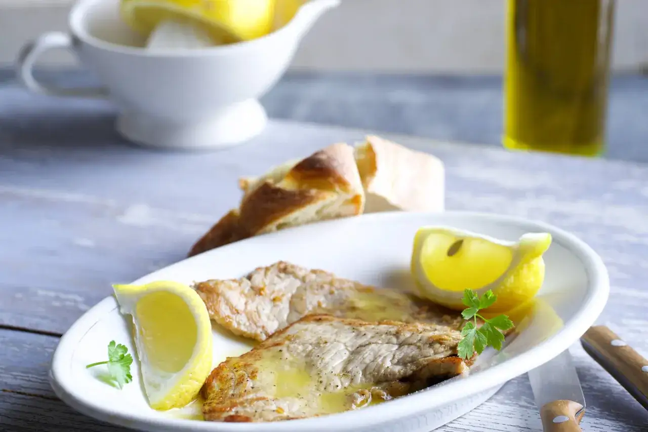Zarte Scaloppine al Limone mit Zitronenspalten, Brot und Oliven&ouml;l.
