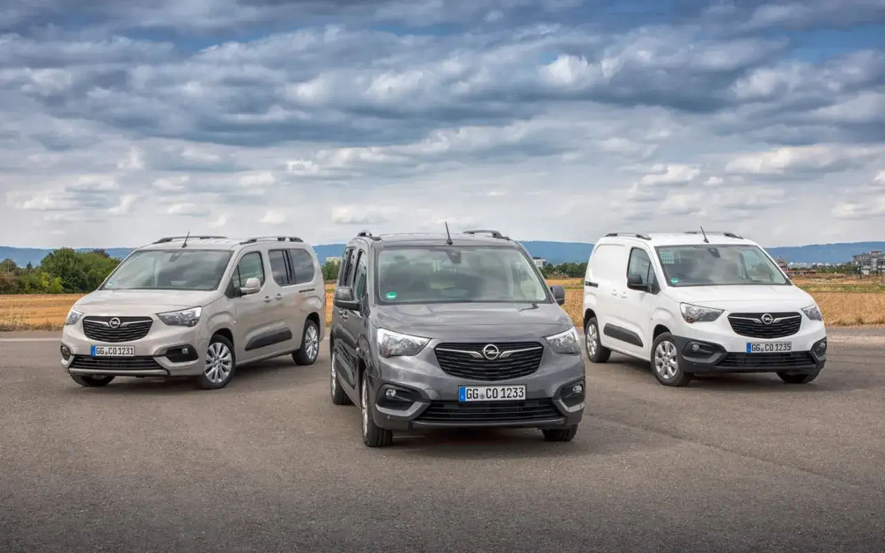 Trzy samochody Opel Combo Life w różnych kolorach: jasnoszary, ciemnoszary i biały, stoją na drodze pod pochmurnym niebem.
