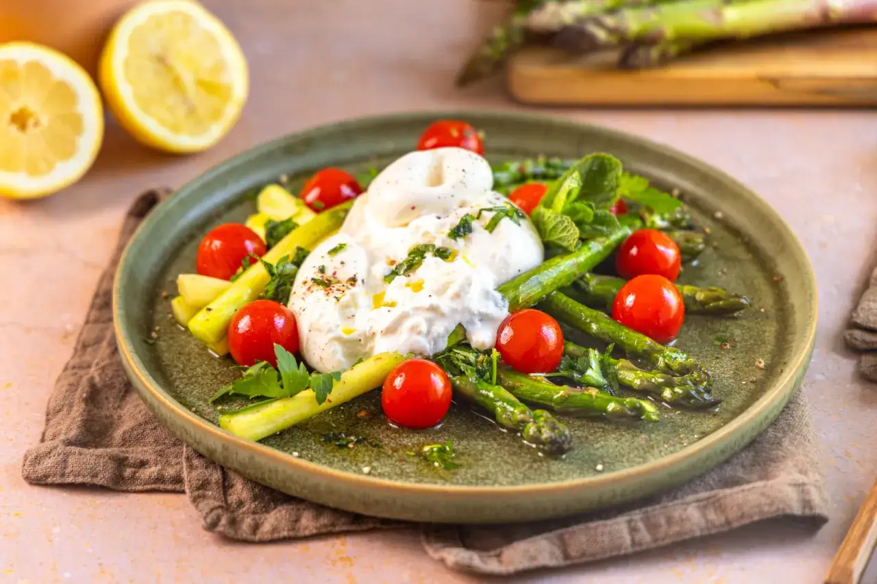 Spargel mal anders: Grüner Spargel mit Kirschtomaten und cremigem Burrata auf einem Teller, garniert mit Kräutern und Zitrone.