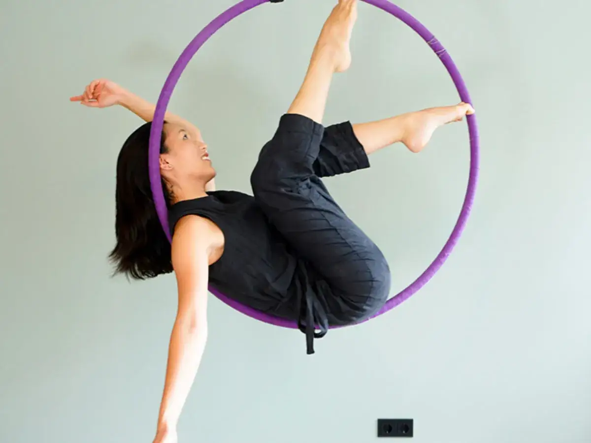 Kobieta wykonuje skomplikowane **aerial hoop figury**, balansując w fioletowej obręczy.