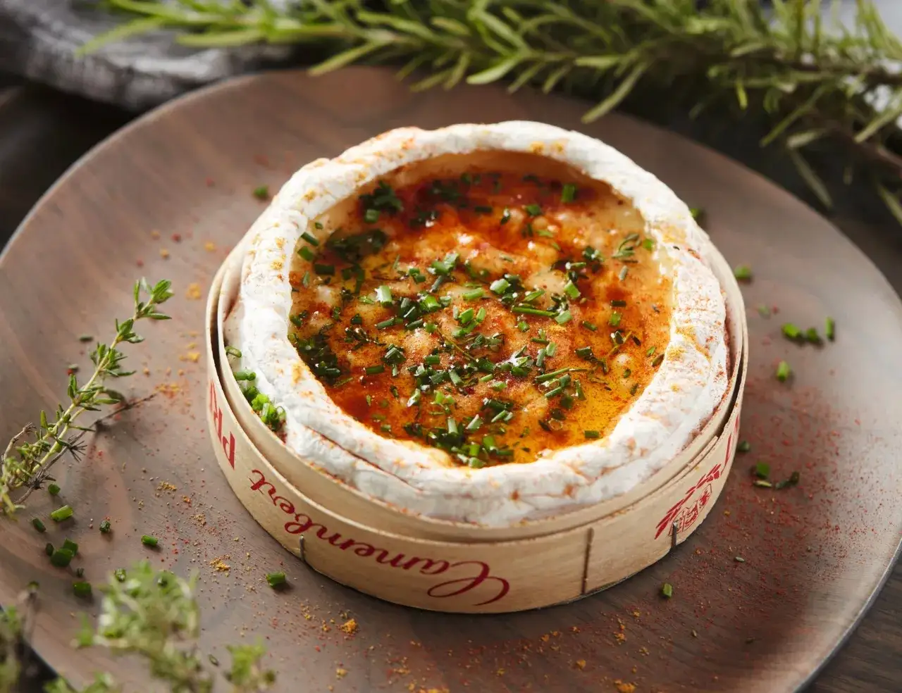 Un camembert au barbecue, fondant et doré, parsemé de ciboulette fraîche et d'épices, prêt à être dégusté.
