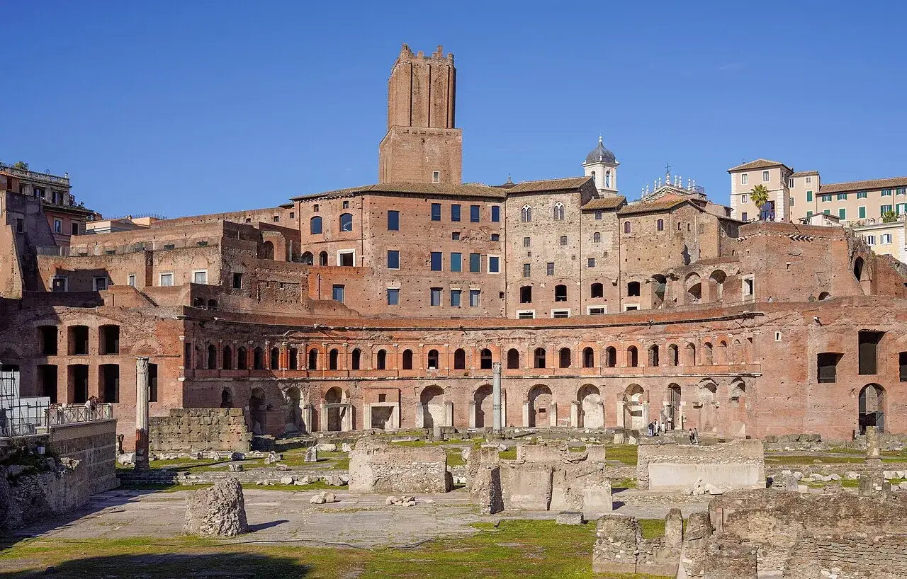 Antiche rovine del **Mercado Trajano** a Roma, con edifici in mattoni rossi e un cielo azzurro.