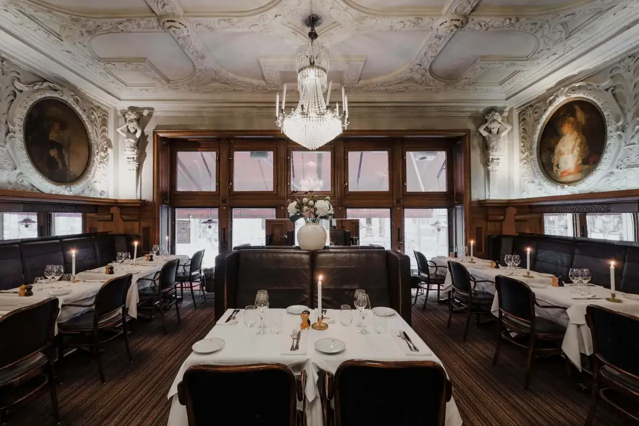 Elegant dukade bord med levande ljus i en av Stockholms gamla restauranger. Kristallkrona i taket och konstverk p&aring; v&auml;ggarna bidrar till den klassiska atmosf&auml;ren.