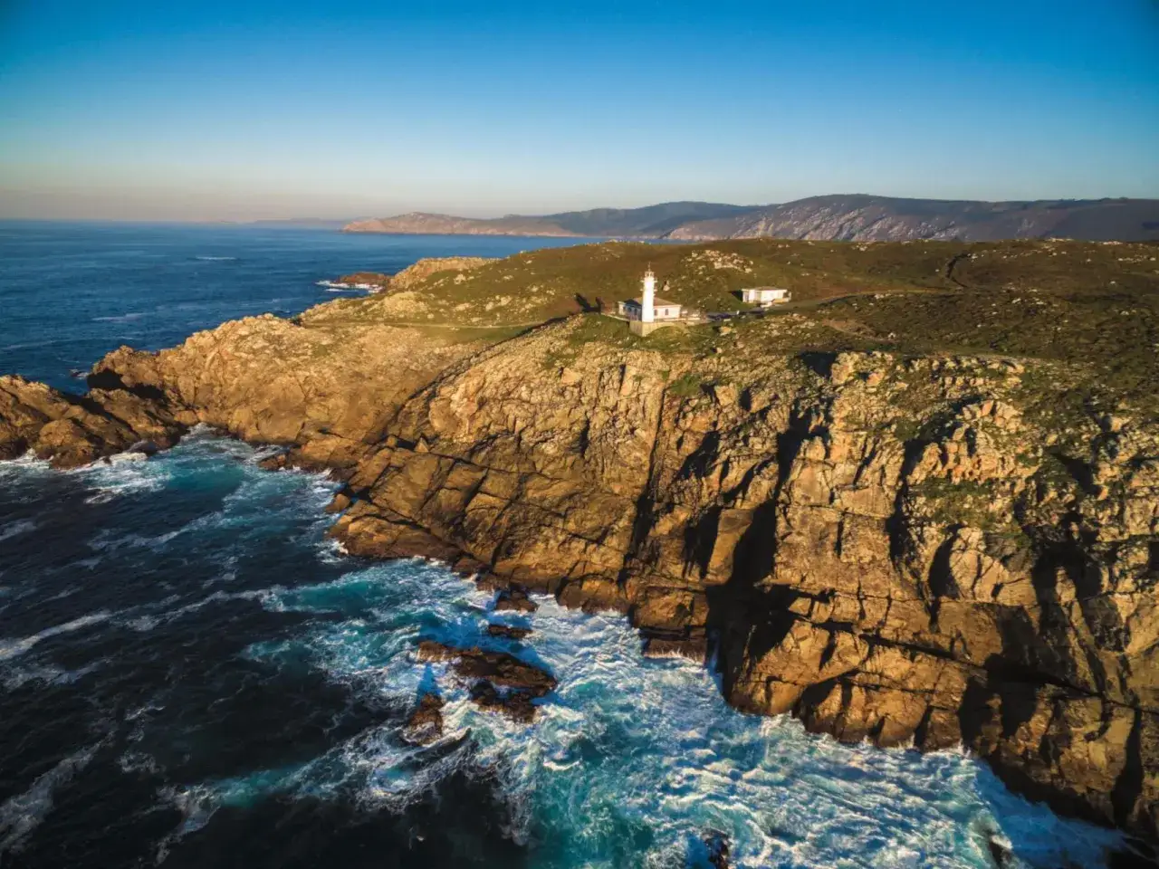 El faro blanco se alza en el cabo Touri&ntilde;&aacute;n, vigilando las rocas escarpadas y el mar azul.