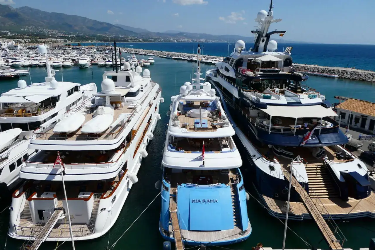 Luksusowe jachty cumują w słonecznym Puerto Banús. W tle góry i błękitne morze.