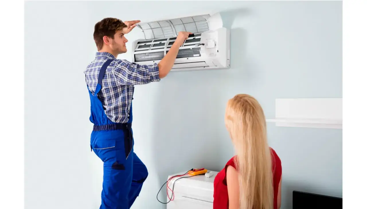 Técnico realiza revisión de aire acondicionado mientras una mujer observa.