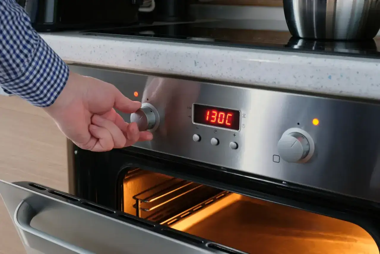 Ręka kręci pokrętłem piekarnika, ustawiając temperaturę 130°C. Przygotowanie do pasteryzowania słoików w piekarniku.