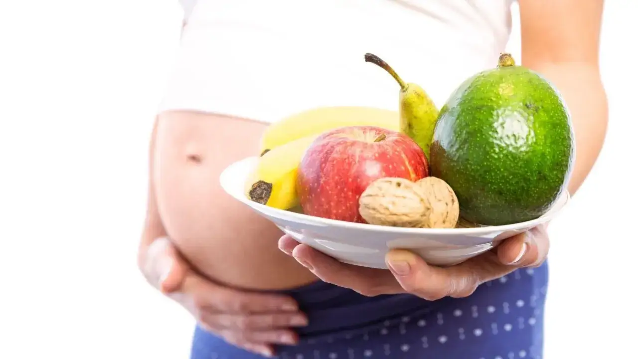 Une femme enceinte tient une assiette de fruits et noix, une alimentation saine pour éviter les problèmes de laxatif enceinte.