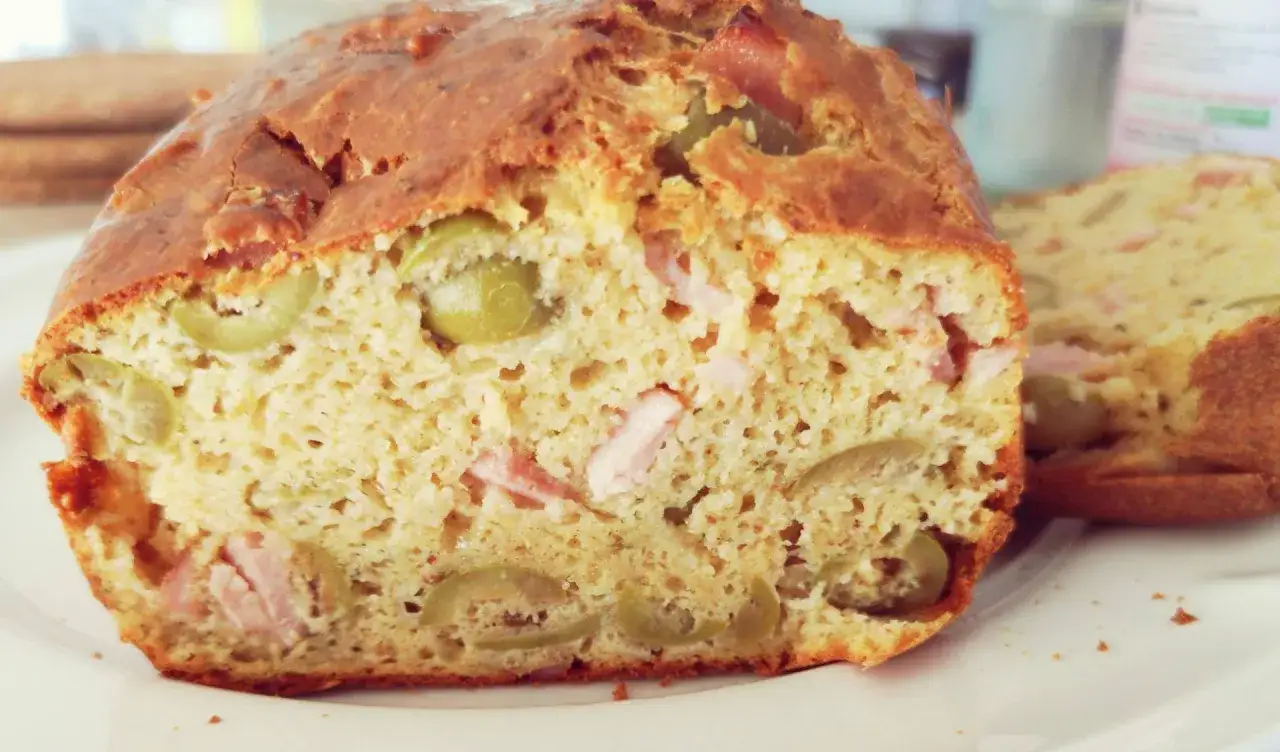 Gros plan sur une tranche de cake sal&eacute; v&eacute;g&eacute;tarien aux olives vertes et morceaux de jambon.