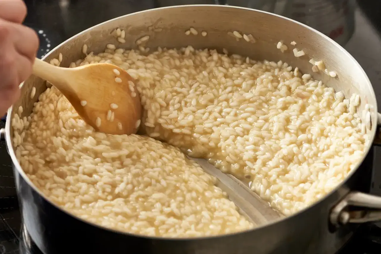 Cuchara de madera removiendo un cremoso arroz italiano en una olla.