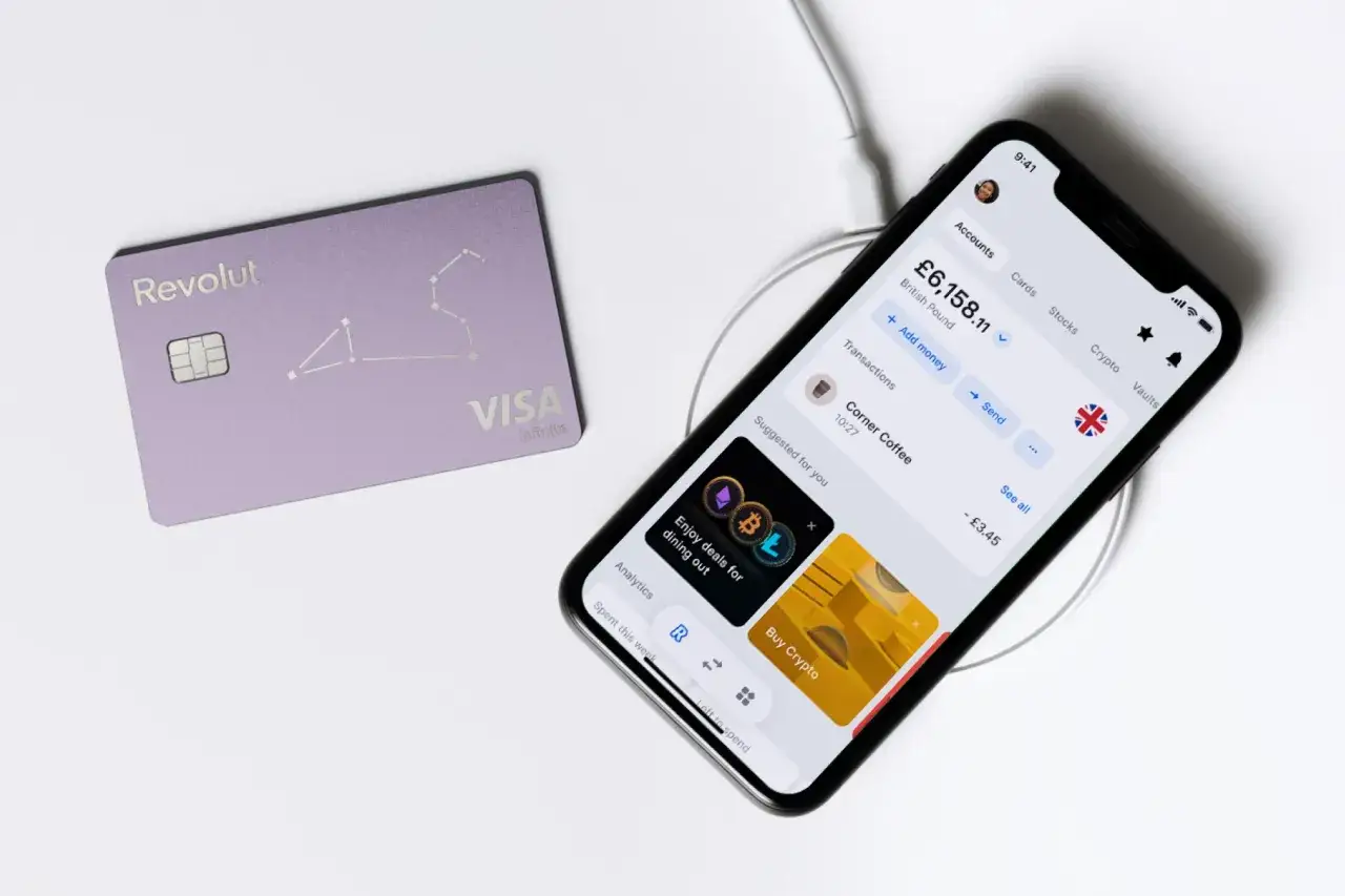 Fioletowa karta Revolut i smartfon z aplikacją finansową, pokazującą saldo i transakcje.