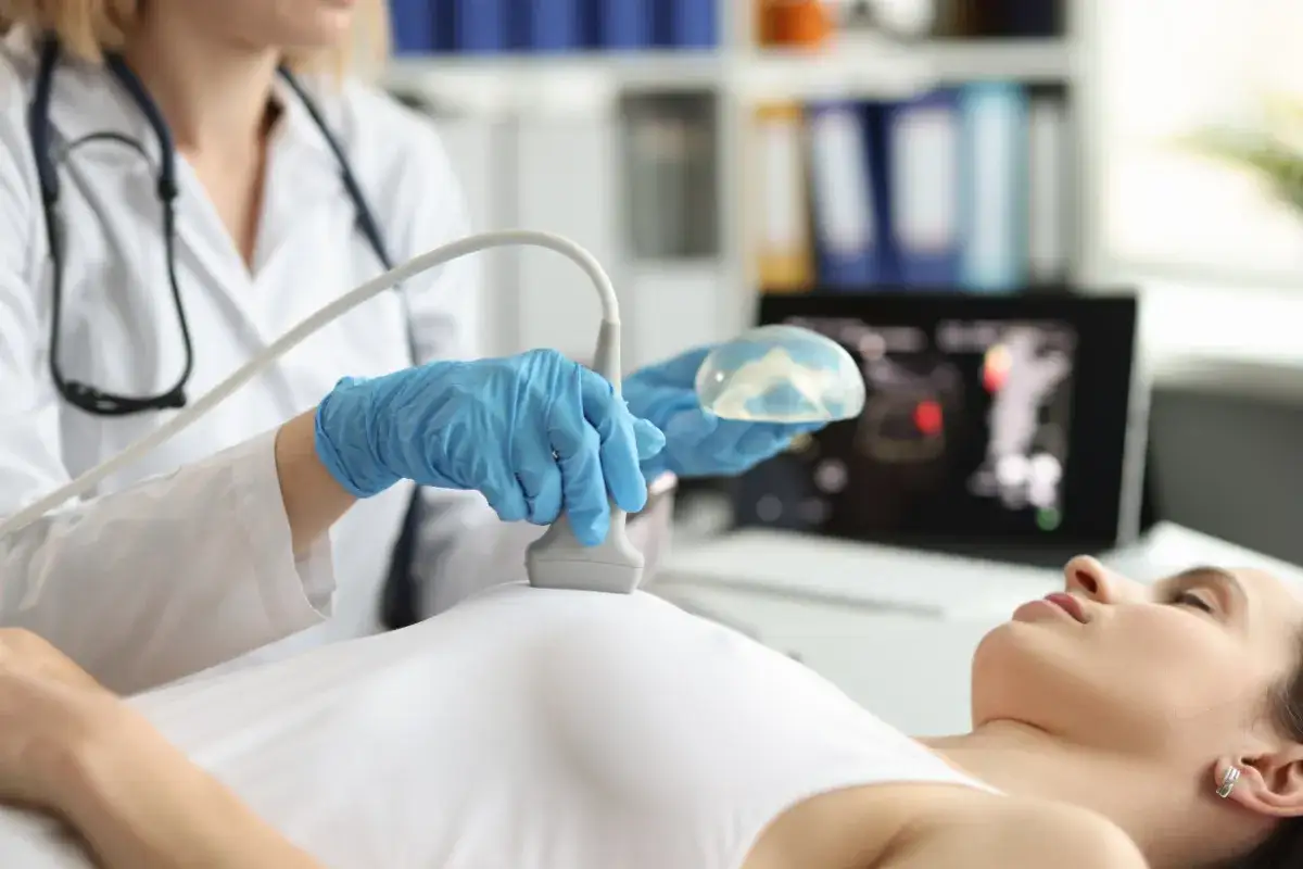 Lekarz wykonuje USG piersi po operacji oszczędzającej, trzymając implant.