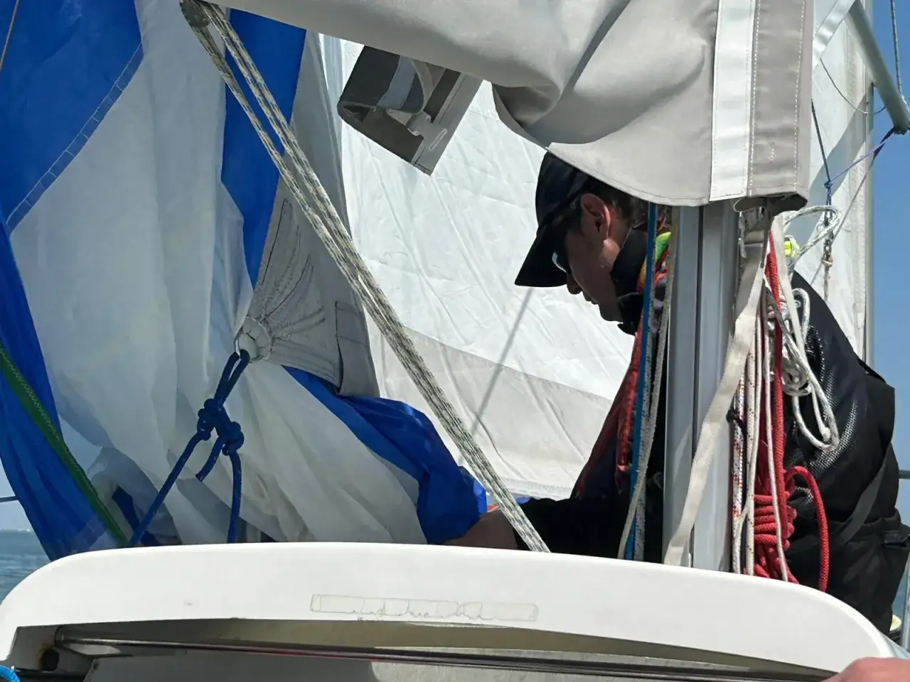 Un velista prepara lo spinnaker a Cattolica, con vele bianche e blu pronte a gonfiarsi al vento.