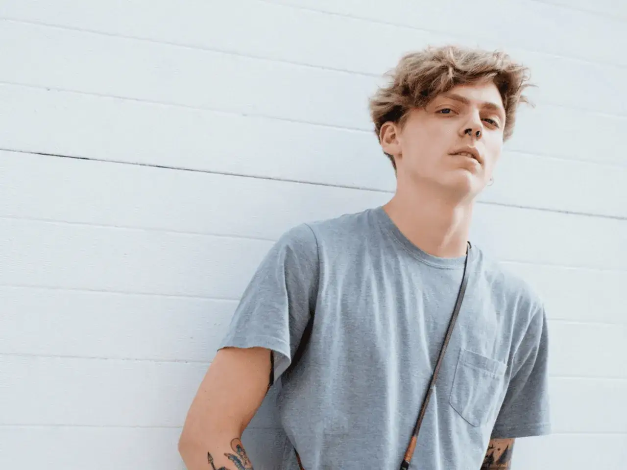 Jeune homme aux cheveux blonds décoiffés, portant un t-shirt gris. Il a un piercing au nez. Attention à la poudre coiffante homme danger pour un style audacieux.