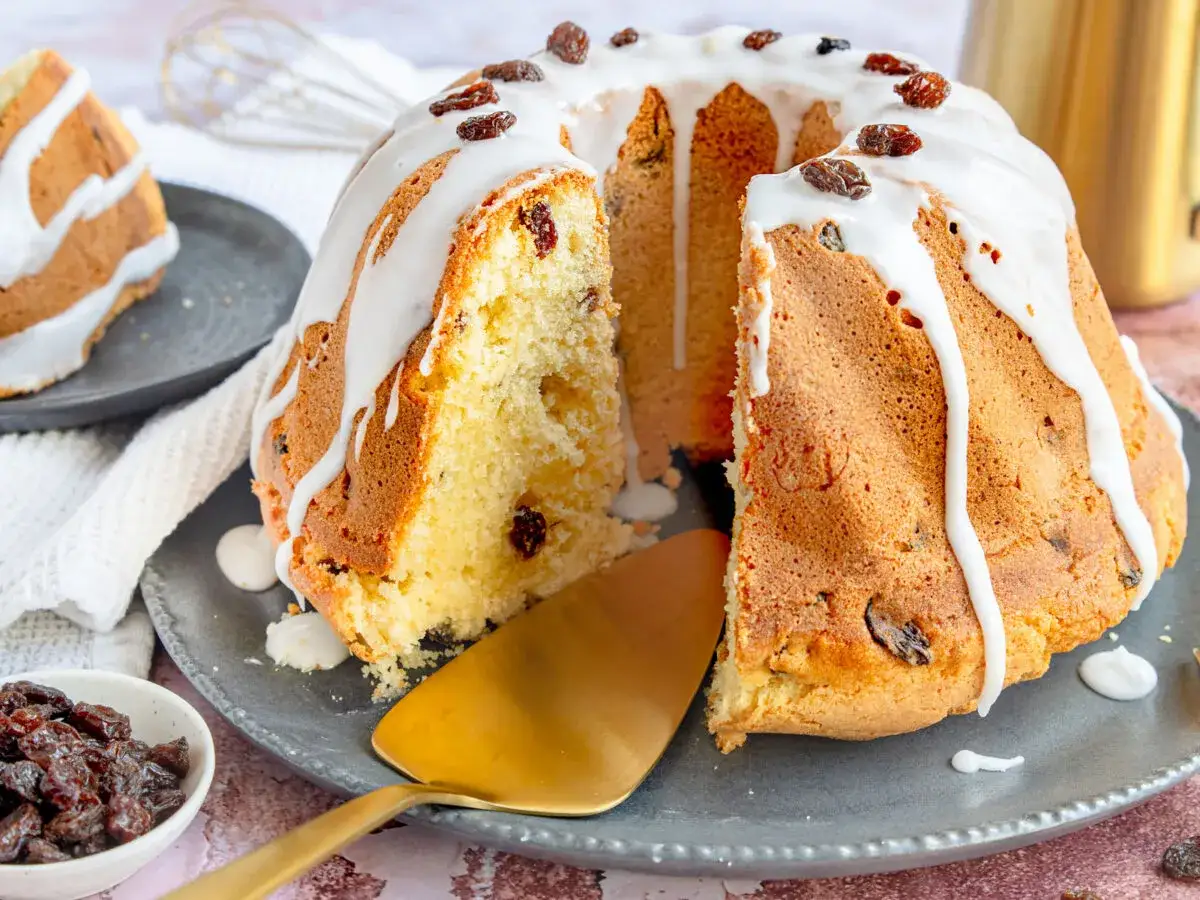 Ein saftiger Rodonkuchen mit Rosinen, &uuml;berzogen mit wei&szlig;er Glasur und garniert mit weiteren Rosinen. Ein St&uuml;ck ist bereits angeschnitten.